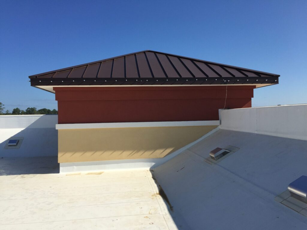 commercial roofing services A rooftop with a red and beige structure, topped by a brown metal roof under a clear blue sky.