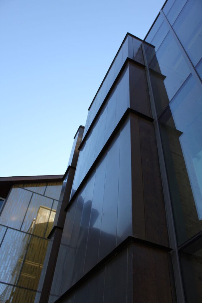 Modern glass and metal building facade viewed from below, against a clear blue sky.