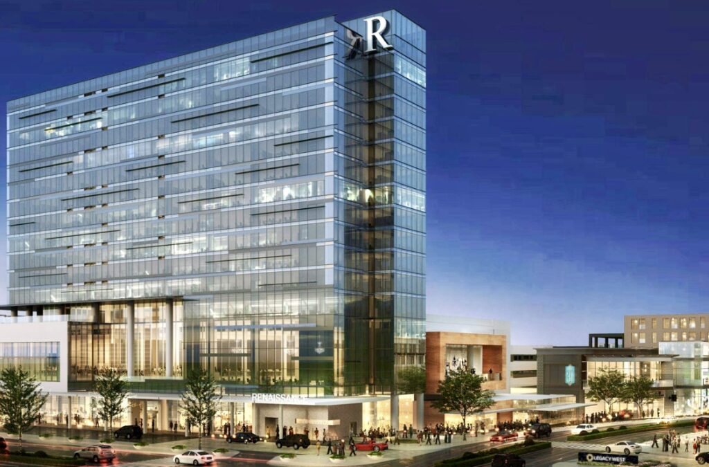 A modern glass building with an R logo, glistening under night lights, showcases its commercial roofing and multiple floors above the bustling street below.